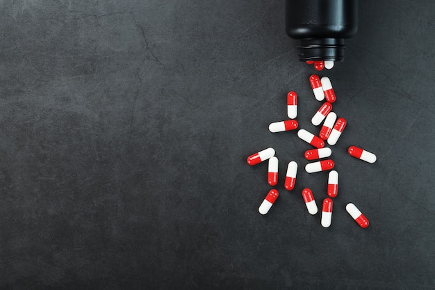 Red and white pills from a black jar on a black background