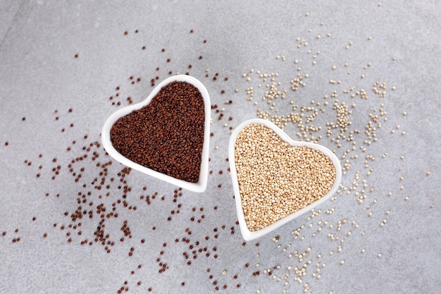 Red and white quinoa in heartshaped bowl on stone background