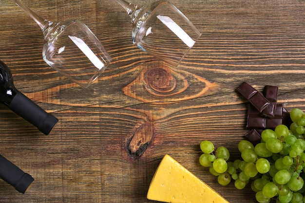 Red and white wine bottles, grape, cheese and glasses over wooden table. Top view with copy space. Still life. Flat lay