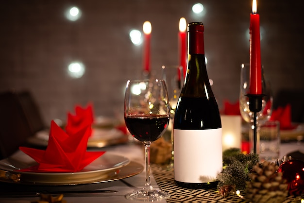 Bottiglia di vino rosso su una tavola festiva per le vacanze di natale con vino un bicchiere su decorazioni lucide rosse e dorate