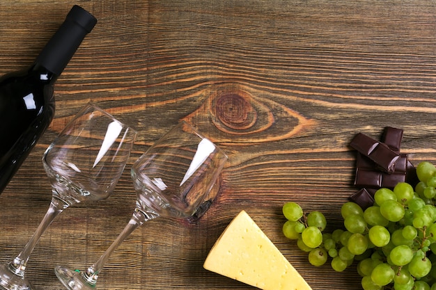 Red wine bottle, grape, cheese and glasses over wooden table. Top view with copy space. Still life. Flat lay