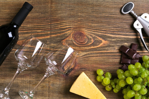 Red wine bottle, grape, cheese and glasses over wooden table. Top view with copy space. Still life. Flat lay