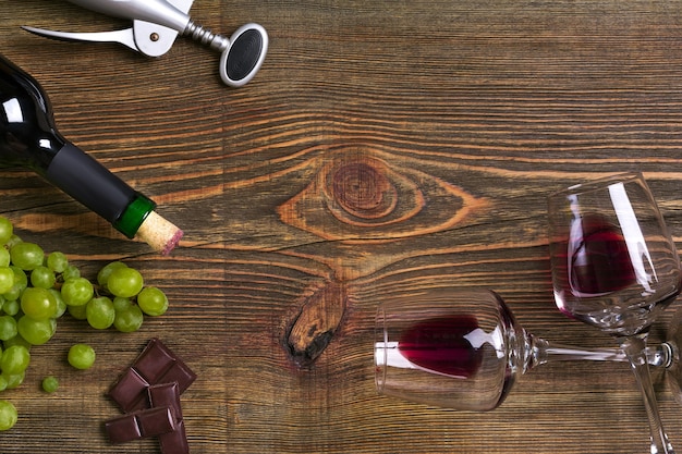 Red wine bottle, grape, chocolate and glasses over wooden table. Top view with copy space. Still life. Flat lay