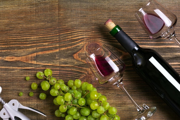 Бутылка красного вина, виноградный шоколад и бокалы над деревянным столом с копией пространства