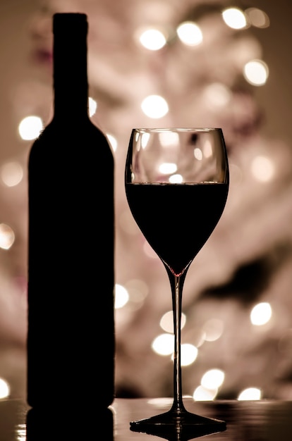 백그라운드에서 크리스마스 트리에 흐릿한 조명이 있는 레드 와인 및 병 실루엣