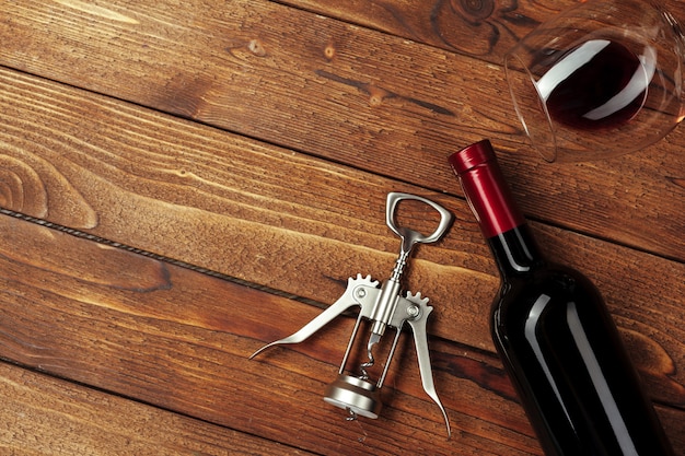 Photo red wine bottle, wine glass and corkscrew on wooden table background