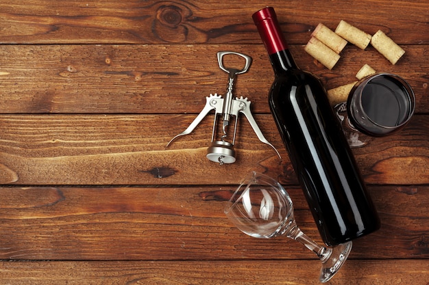 Red wine bottle, wine glass and corkscrew on wooden table background