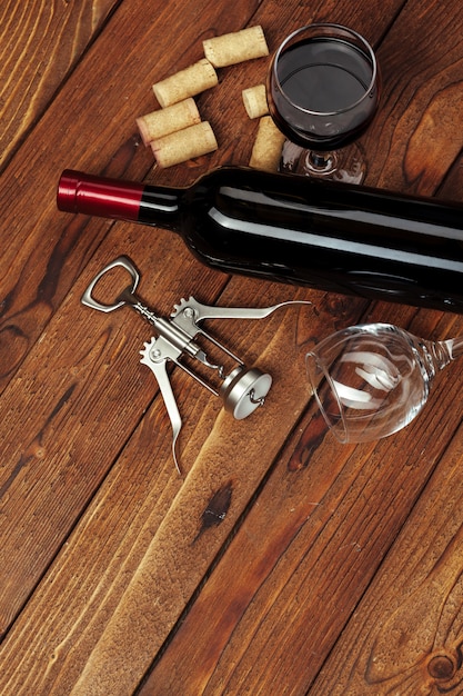 Foto bottiglia di vino rosso, bicchiere di vino e cavatappi sul tavolo di legno