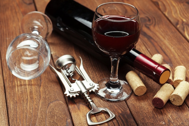 Red wine bottle, wine glass and corkscrew on wooden table