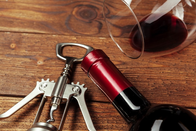 Red wine bottle, wine glass and corkscrew on wooden table