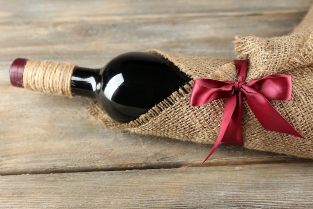 Red wine bottle wrapped in burlap cloth on wooden planks background