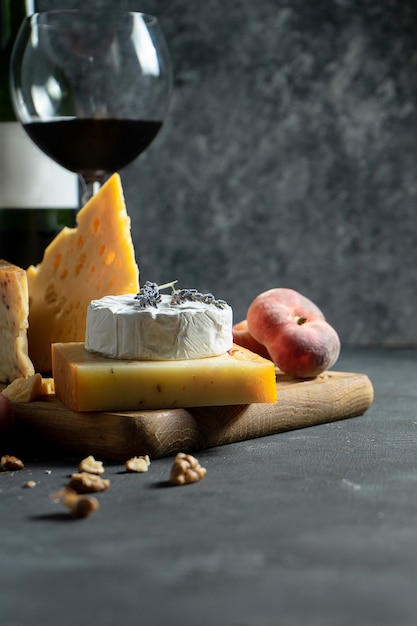 Red wine and cheese. Different types of cheese with nuts, lavander and fig peach on cutting board. Romantic dinner. Copy space for design. Dark background. Soft focus