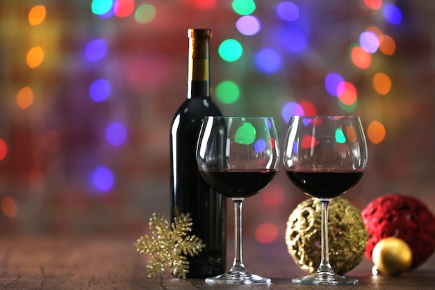 Red wine and Christmas ornaments on wooden table on Christmas lights surface