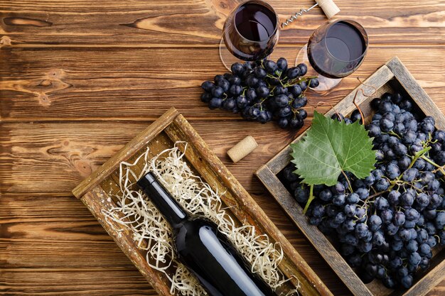 red wine composition on brown wooden table. top view. red wine bottle corkscrew corks wine glasses black ripe grapes in box on wooden table. flat lay copy space.