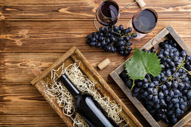 Red Wine composition on brown wooden table. Top view. Red wine bottle corkscrew corks wine glasses black ripe grapes in box on wooden table. Flat lay copy space.