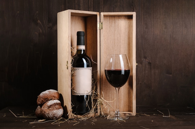 Red wine composition with bread bottle in box and wineglass on brown wooden table