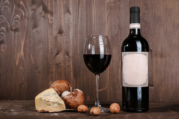 Red wine composition with bread, two bottles in box and wineglass on wooden table