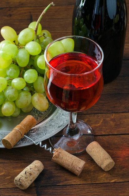 Red wine in glass, bunch of grapes in an antique plate and corkscrew on wooden table. ÃÂ¡lose-up.