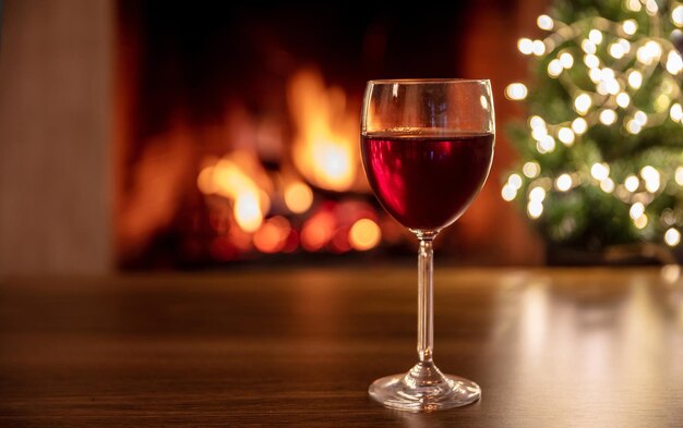 Red wine glass burning fireplace background Christmas tree bokeh lights decoration