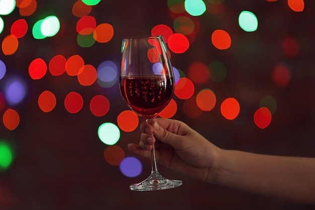 Бокал красного вина в женской руке на фоне боке