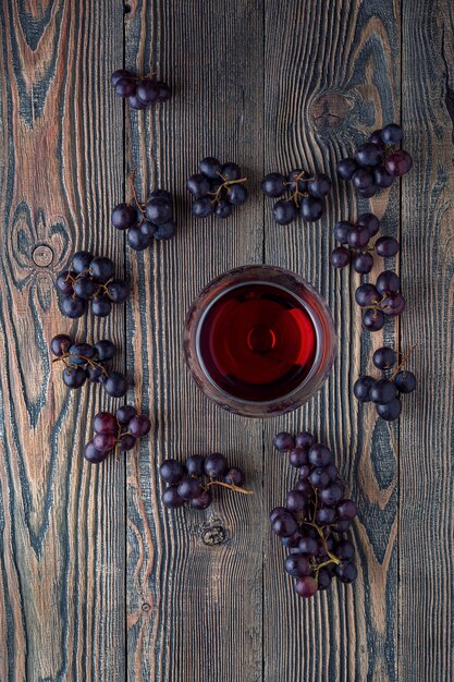 Red wine in a glass and grapes on an old wooden table. Top view.