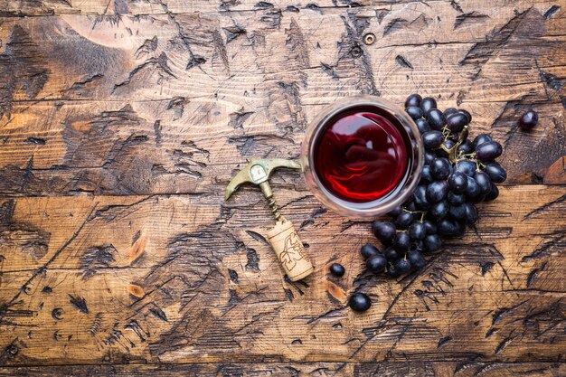 Red wine in a glass and ripe grapes on wooden background, top view