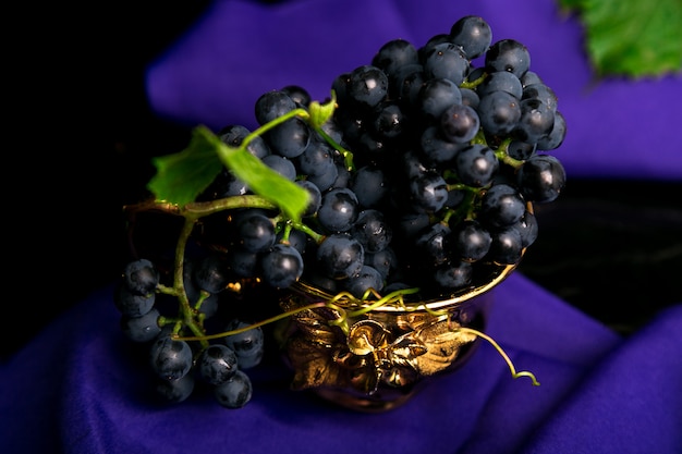 Red wine grapes in golden cup on violet .