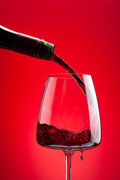 Red wine pouring from bottle into glass over red background