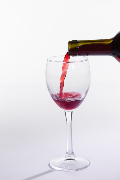 白い背景の上のボトルからガラスに注ぐ赤ワイン