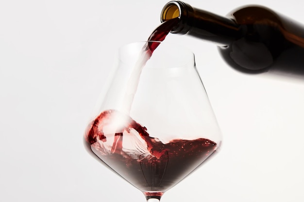 Red wine pouring into tilted wineglass from bottle