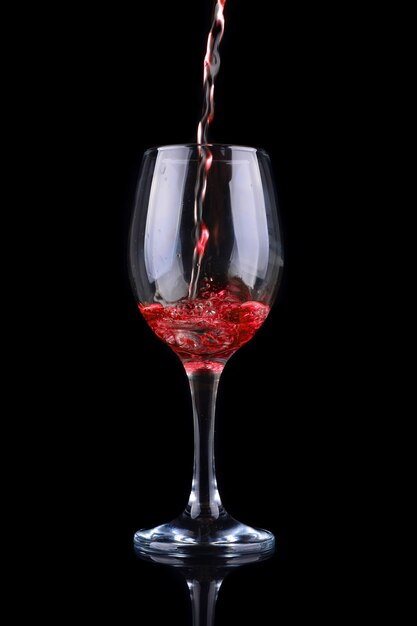 Red wine pouring into a wine glass. Isolated on black background