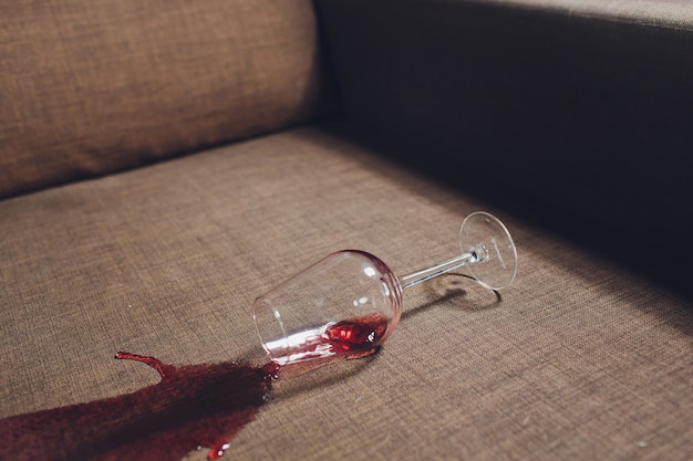 Красное вино пролилось на диван серого дивана.