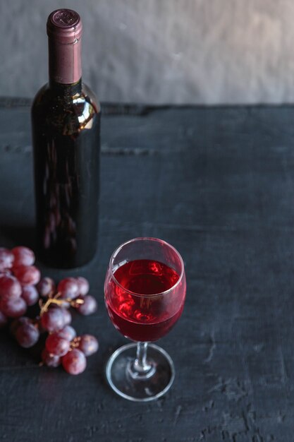 Red wine and wine bottle with grapes on black surface