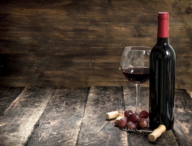 Red wine with a branch of grapes and a corkscrew. On a wooden background.