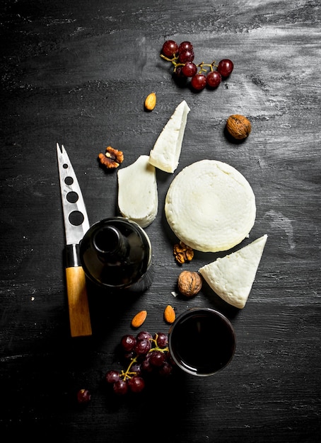 Red wine with fresh sheep cheese and grapes. On a black wooden background