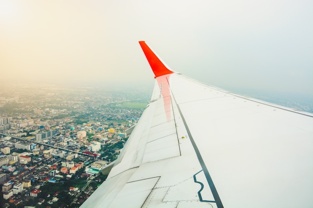 Red wing of the aircraft view from airplane window seat during take off and flying above city landscape 