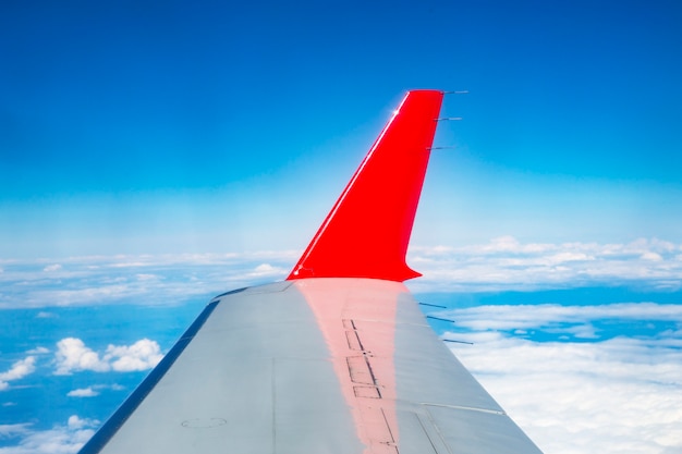 The red wing of the plane on the background of a bright blue sky