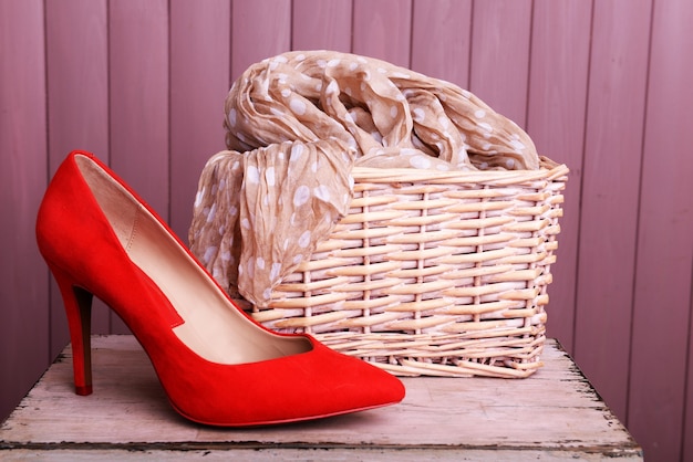 Red women shoes and scarf on bench on wooden background