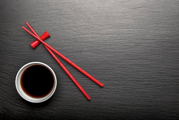 Red wooden chopsticks and bowl of soy sauce on black slate