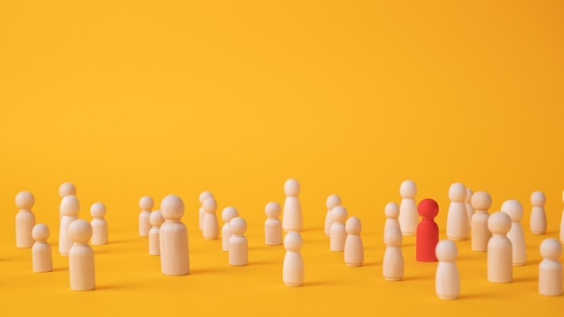 A red wooden figurine of a person is in a crowd of figurines on a yellow background