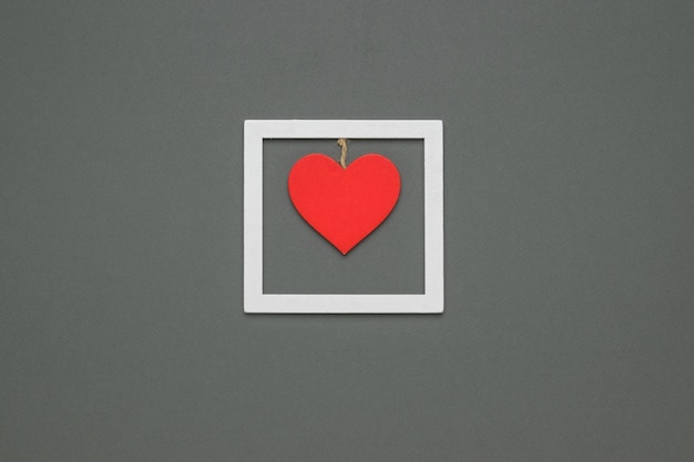 A red wooden heart suspended from a rope on a wooden frame on a gray background The concept of Valentines Day Flat lay