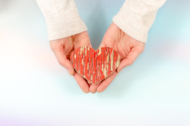 Red wooden heart in woman's hands female hands hold heart on delicate blue background