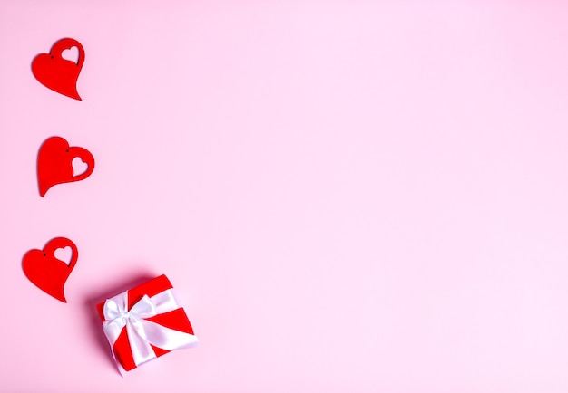 Красные деревянные сердечки и коробка для подарка ко Дню Святого Валентина на розовом