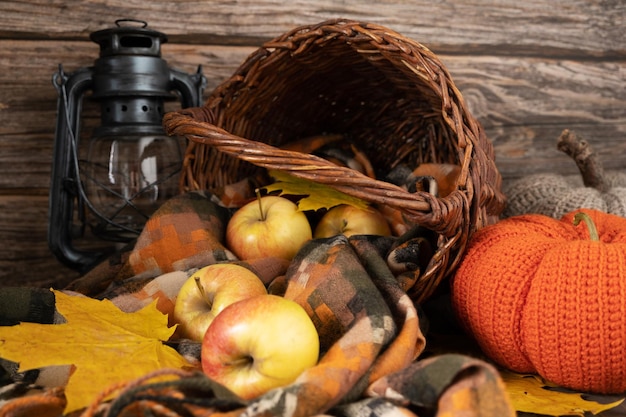 Red yellow apples in a wicker basket next to a knitted pumpkin and a kerasin lantern