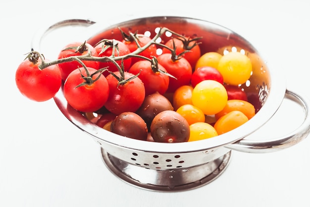 Red, yellow and black cherry tomatoes in colander on white