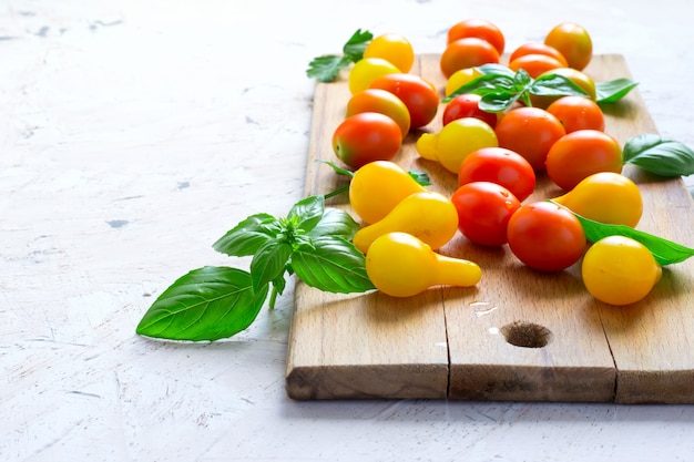 Red and yellow cherry tomatoes on a cutting board with basil lea