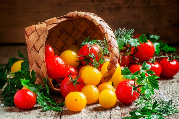 Red and yellow cherry tomatoes spill out of a wicker basket vintage wooden background country style selective focus