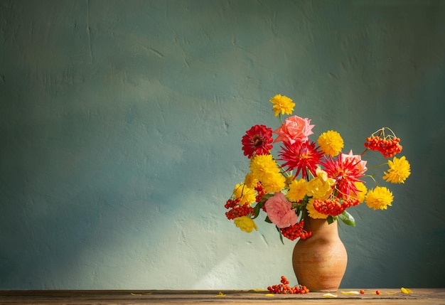 Red and yellow flowers on jug in sunlight on background dark wall