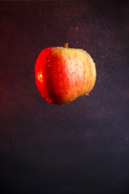 Foto grande mela rosso-gialla, inondata d'acqua su uno sfondo scuro