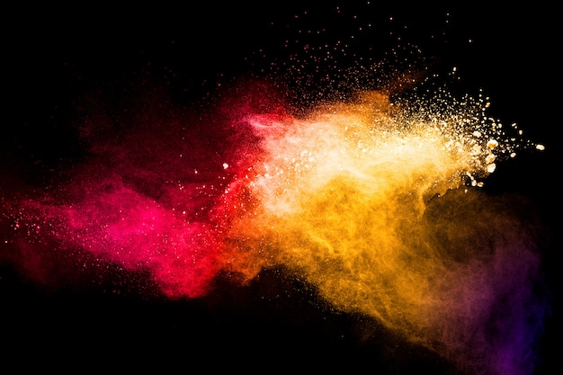 Red yellow powder explosion cloud on black background. Freeze motion of red yellow color dust  particles splashing.